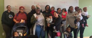 A group of 9 young Oakland Promise parents & their children giving thumbs up to the camera at a community event